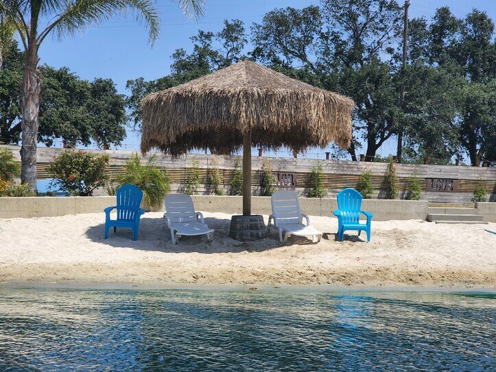 A private white-sand beach site with a shade palapa, lounge chairs, and the lake